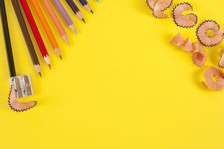 Some colored pencils of different colors and a pencil sharpener and pencil shavings on the yellowの写真素材