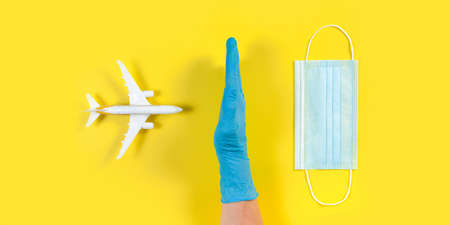 Plane model and face medical mask on a yellow background. Doctor hand with gloveの写真素材