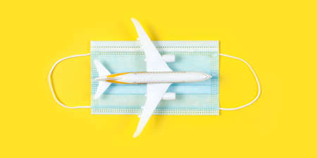 Plane model and face mask on a yellow background. Flight impact of coronavirus (COVID-19) concept.の写真素材