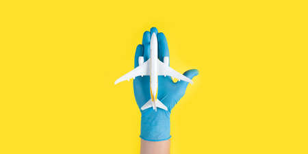 Hand in glove holding model airplanes on yellow background. Concept traveling. Copy spaceの写真素材