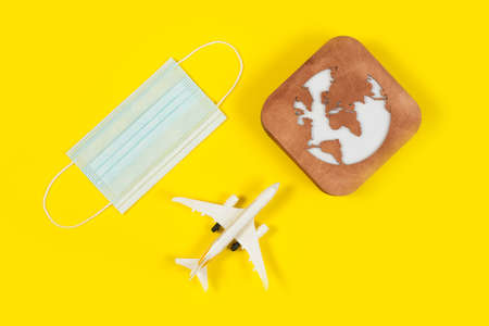 Plane model, face mask and earth model on a yellow background. Flight impact of coronavirus (COVID-19) concept.の写真素材