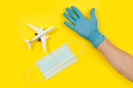 Plane model and face medical mask on a yellow background. Doctor hand with gloveの写真素材