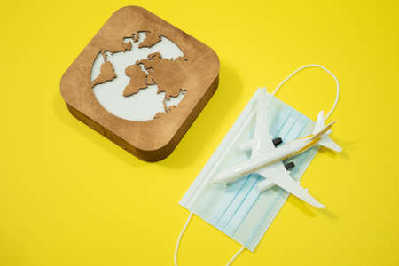 Plane model, face mask and earth model on a yellow background. Flight impact of coronavirus (COVID-19) concept.の写真素材