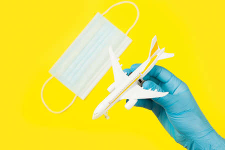 Hand in glove holding model airplane over face mask. Air travel resumes after travel. Open borders, quarantine end.の写真素材