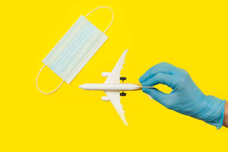 Hand in glove holding model airplane over face mask. Air travel resumes after travel. Open borders, quarantine end.の写真素材