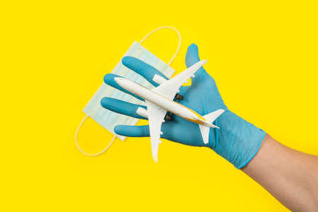 Hand in glove holding model airplane over face mask. Air travel resumes after travel. Open borders, quarantine end.の写真素材