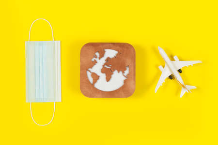 Plane model, face mask and earth model on a yellow background. Flight impact of coronavirus (COVID-19) concept.の写真素材