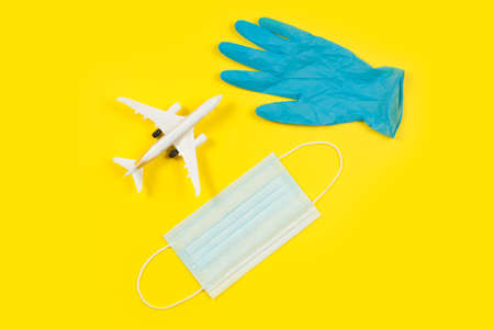Plane model and face medical mask on a yellow background. Doctor hand with gloveの写真素材