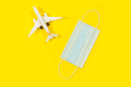 Plane model and face mask on a yellow background. Flight impact of coronavirus (COVID-19) concept.の写真素材