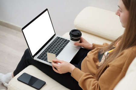 Beautiful girl holding gold credit card in hands and using laptop computer to perform shopping online by inputting card information for payment method. Ecommerce business concept.の写真素材