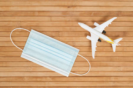 Plane model and face mask on a wooden background with copy space. resumption of flights. opening of...