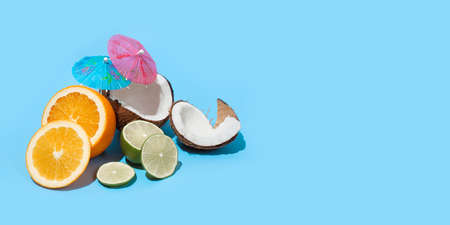Fresh juicy orange, coconut and green lime with a cocktail umbrella isolated on blue background. Concept of Healthy eating and dieting. Travel and holiday concept. Copy space. Free space for your textの写真素材