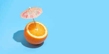 Fresh juicy orange with a cocktail umbrella isolated on blue background. Concept of Healthy eating and dieting. Drink conceptの写真素材