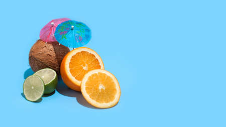 Fresh juicy orange, coconut and green lime with a cocktail umbrella isolated on blue background. Concept of Healthy eating and dieting. Travel and holiday conceptの写真素材