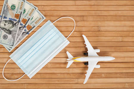 Plane model, face mask and money on a wooden background with copy space. resumption of flights. opening of international flights after concept of coronavirus (COVID-19).の写真素材