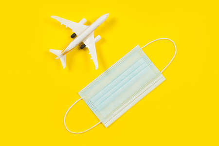 Plane model and face mask on a yellow background. Flight impact of coronavirus (COVID-19) concept.の写真素材
