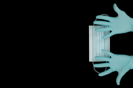 close up of doctor's hand in blue gloves with a medical face mask for protection against infection on black background. Covid. Coronavirusの写真素材