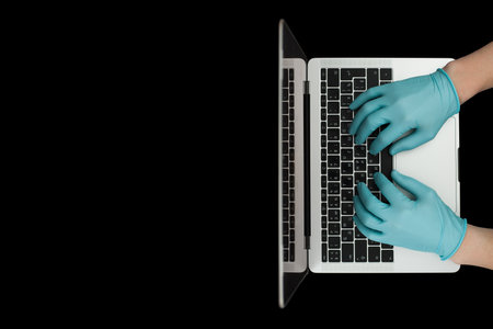 Hands in blue protective gloves typing on laptop keyboard. Top view.の写真素材