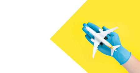 Hand in glove holding model airplanes on yellow background. Concept traveling. Copy spaceの写真素材
