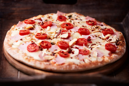 Pizza with ham, mozzarella cheese and cherry tomatoes on wooden backgroundの写真素材