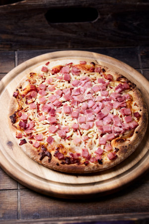 Pizza with ham and cheese on a wooden board, selective focusの写真素材