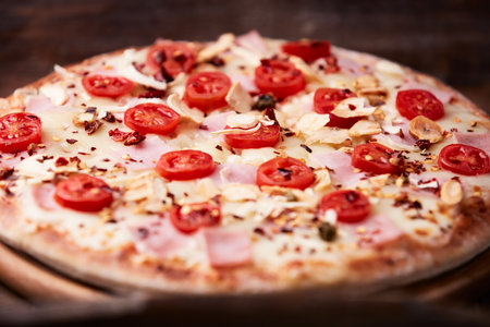 Pizza with ham, tomatoes and cheese on a dark wooden backgroundの写真素材