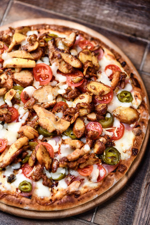 Pizza with meat, vegetables and cheese on a wooden background.の写真素材