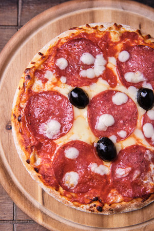 Pizza with salami, mozzarella and olives on wooden backgroundの写真素材