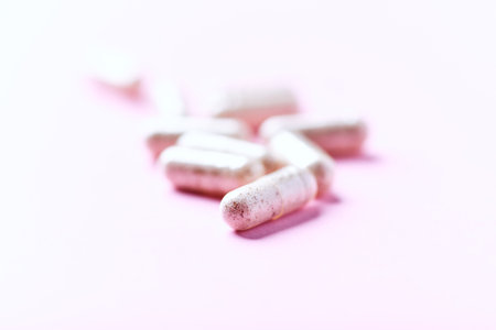 Heap of white pills on pink background. Focus on foreground.