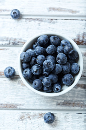 Fresh blueberries in bowl on white wooden background. Selective focus.