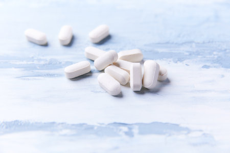 Pile of white pills on light blue wooden background, closeup
