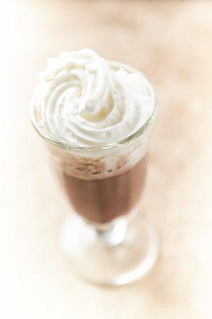 Iced coffee with whipped cream in glass on wooden table background.