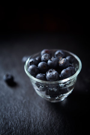 Fresh blueberries in a glass bowl on a black slate background.の写真素材