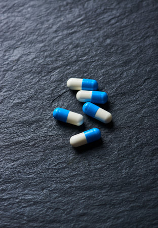 Capsules of blue and white pills on a dark background.の写真素材