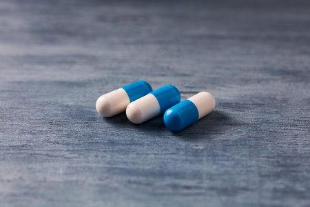 White and blue pills on wooden background. Focus on foreground, soft bokeh.の写真素材