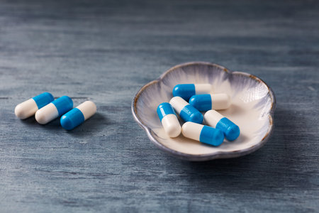 Blue and white pills in a bowl on a blue wooden background.の写真素材