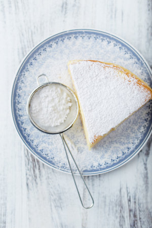 Cake with sugar powder on a plate on a white wooden backgroundの写真素材