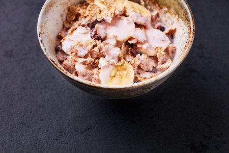 Bowl of oat flakes with banana and raisins on dark backgroundの写真素材