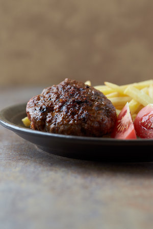 Grilled hamburger with french fries and vegetables on a dark background