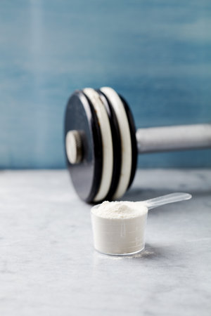 Whey protein powder in a measuring spoon and a dumbbell.の写真素材