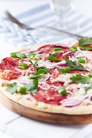 Pizza with salami, onion and parsley on a white wooden backgroundの写真素材