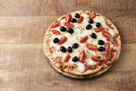 Pizza with mozzarella, tomatoes and black olives on wooden backgroundの写真素材