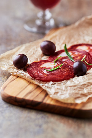 Slices of salami with olives and rosemary on wooden boardの写真素材