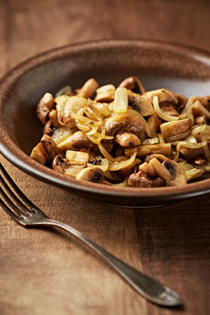 Fried mushrooms with onions and garlic in a plate on a wooden tableの写真素材