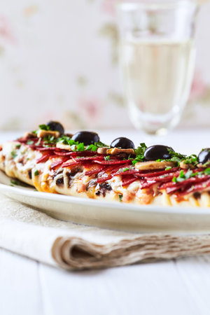 Pizza with salami, mozzarella and olives on a white background.