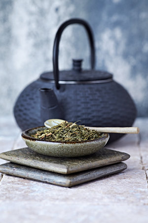 Dry tea leaves in ceramic bowl and teapot on wooden tableの写真素材