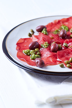 Marbled beef carpaccio with green olives and capersの写真素材
