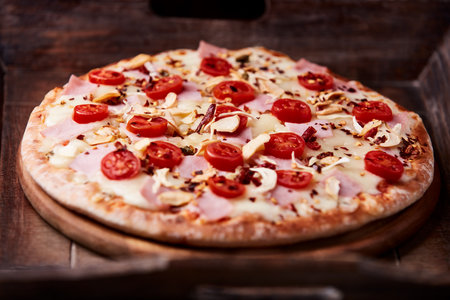 Pizza with ham, mozzarella and cherry tomatoes on wooden backgroundの写真素材