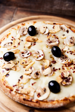 Pizza with mushrooms, olives and cheese on a wooden tableの写真素材