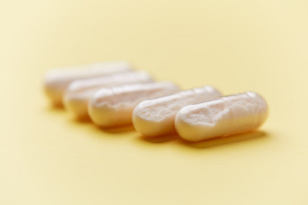 Closeup of white pills on yellow background. Focus on foreground.